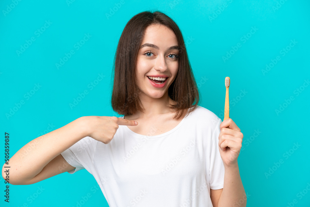 Young Ukrainian woman brushing teeth isolated on blue background with surprise facial expression Young Ukrainian woman brushing teeth isolated on blue background with surprise facial expression