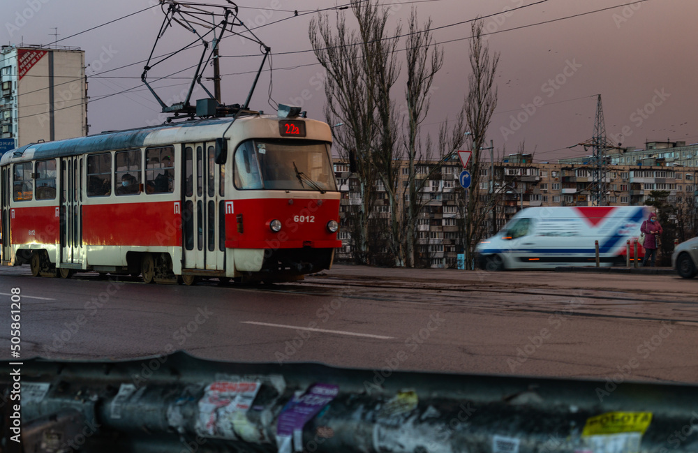 A red tram runs in the middle of the road. Public transport. The tram goes in cloudy weather A red tram runs in the middle of the road. Public transport. The tram goes in cloudy weather