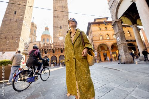 Stylish woman walks the street on background of famous towers in Bologna city. Italian lifestyle and street fashion concept. Idea of traveling Italy