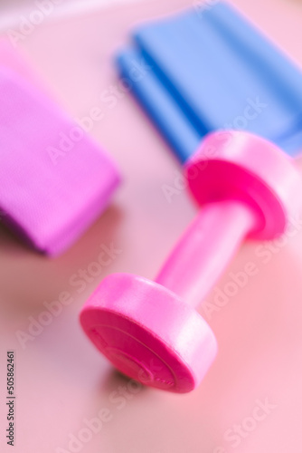 Composizione di attrezzi sa palestra su sfondo rosa. Piccolo manubrio rosa con banda elastica blu e bande di resistenza blu e rosa photo