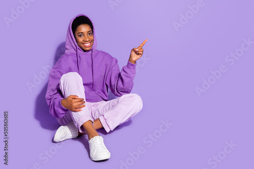 Full length photo of cool millennial lady sit ndex promo wear hoodie trousers shoes isolated on purple background photo