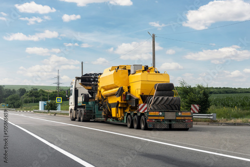 Long heavy industrial truck with semi trailer platform transport disassembled combine harvester machine on common highway on bright summer day. Agricultural equipment transportation service