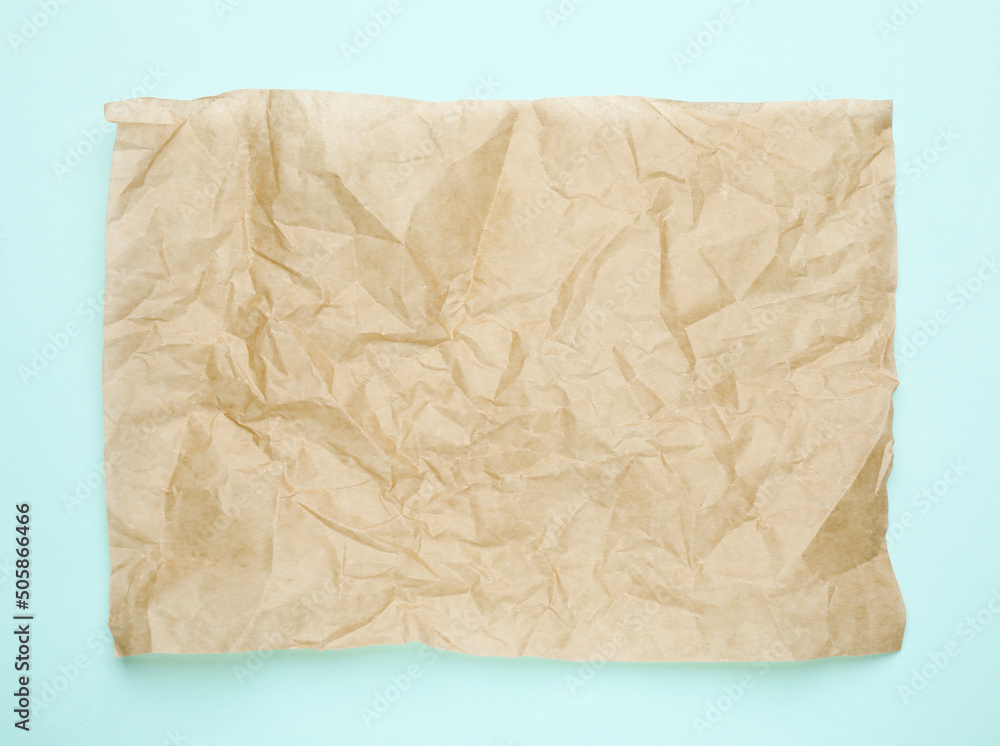 Sheet of crumpled brown baking paper on light blue background, top view