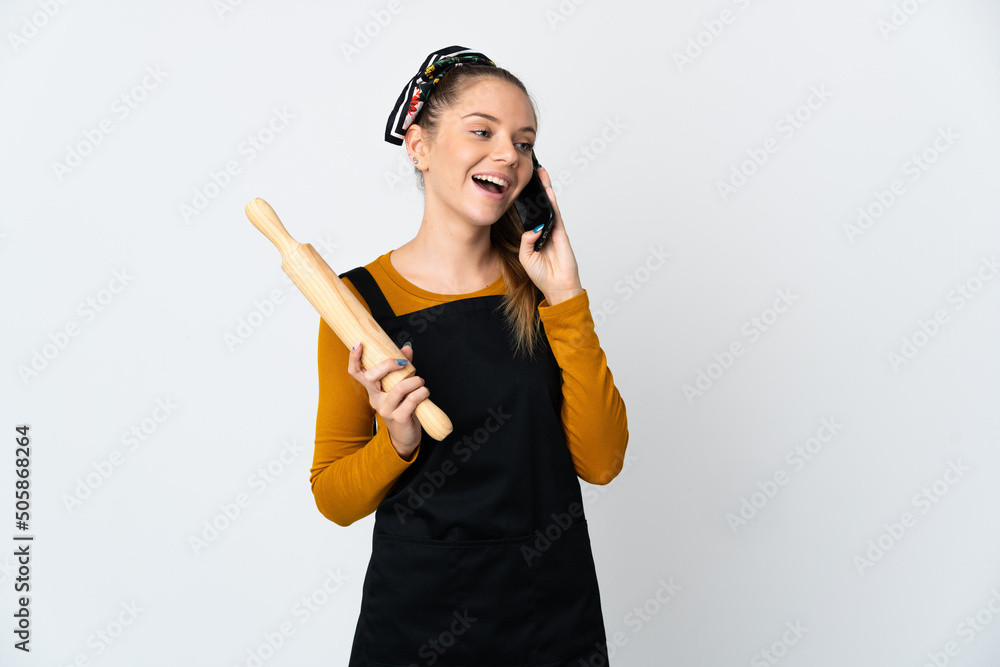 Young Lithuanian woman holding a rolling pin isolated on white background keeping a conversation with the mobile phone Young Lithuanian woman holding a rolling pin isolated on white background keeping a conversation with the mobile phone