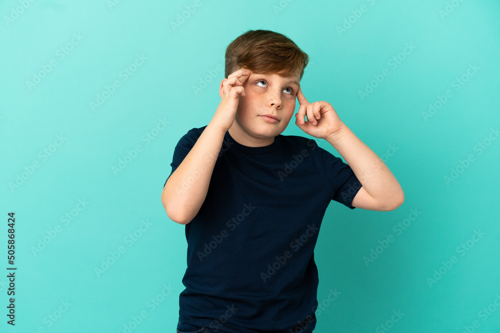 Little redhead boy isolated on blue background having doubts and thinking Little redhead boy isolated on blue background having doubts and thinking