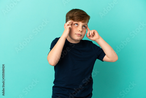 Little redhead boy isolated on blue background having doubts and thinking © luismolinero