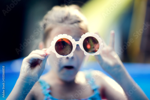 Funny European preteen girl in swimsuit swims with sunglasses