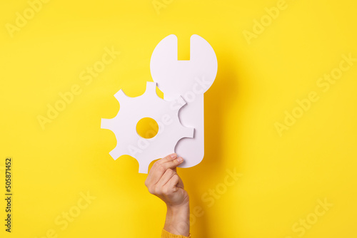 Service tools symbol in hand over yellow background, concept of repair