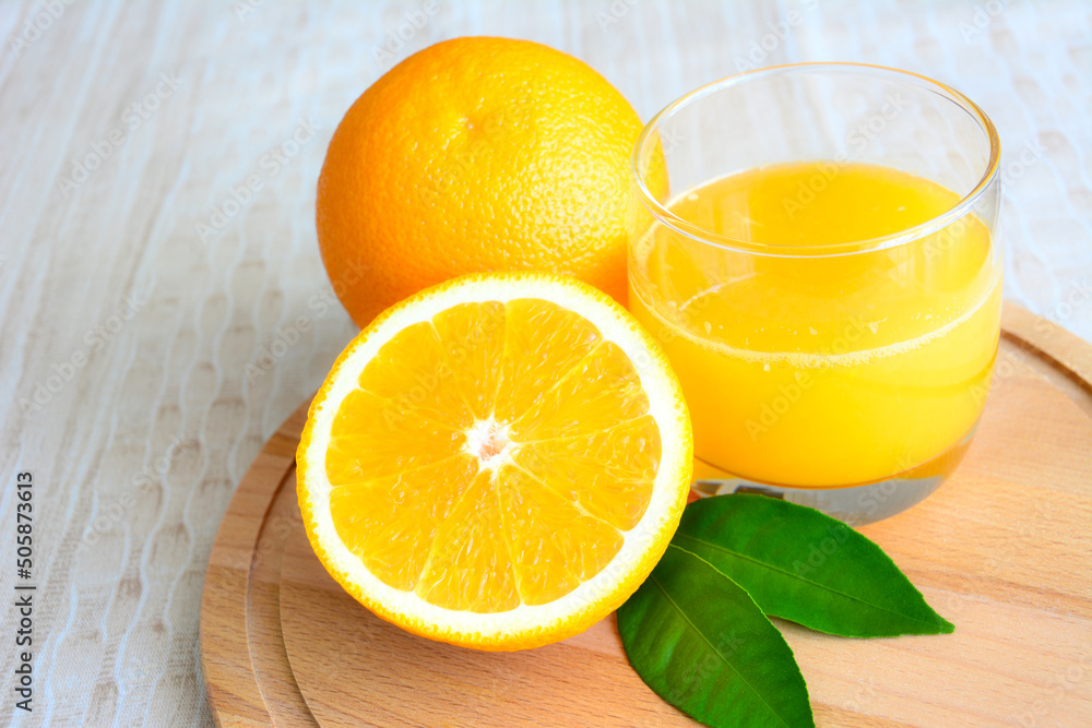 fresh garden oranges with leaves and glass of orange juice on beige background, close-up fresh garden oranges with leaves and glass of orange juice on beige background, close-up