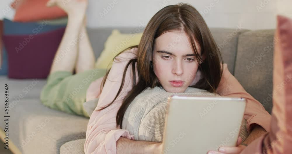 Caucasian non-binary transgender woman lying on sofa, using tablet Caucasian non-binary transgender woman lying on sofa, using tablet