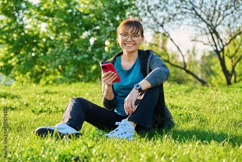 Outdoor portrait of mature smiling woman looking at camera sitting on grass