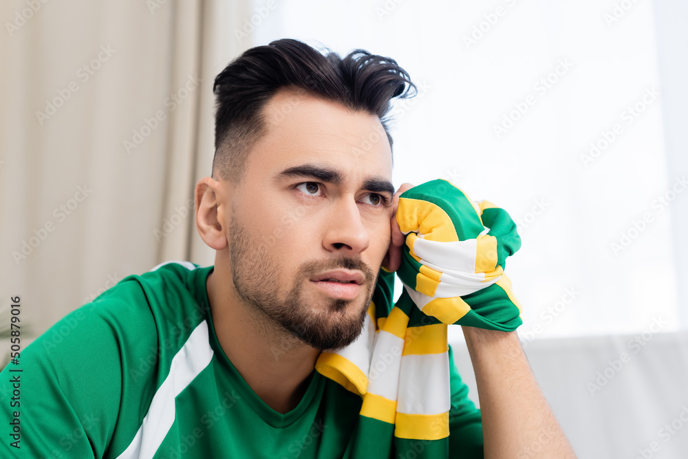 upset man with striped scarf watching sports match at home. upset man with striped scarf watching sports match at home.
