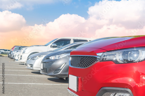 Car parked in large asphalt parking lot with white cloud and blue sky background. Outdoor parking lot travel transportation technology concept. Front view of red cars
