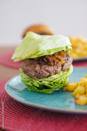 Low carb diet lettuce burger, with caramalized onion and french fries on a table. Selective focus. photo