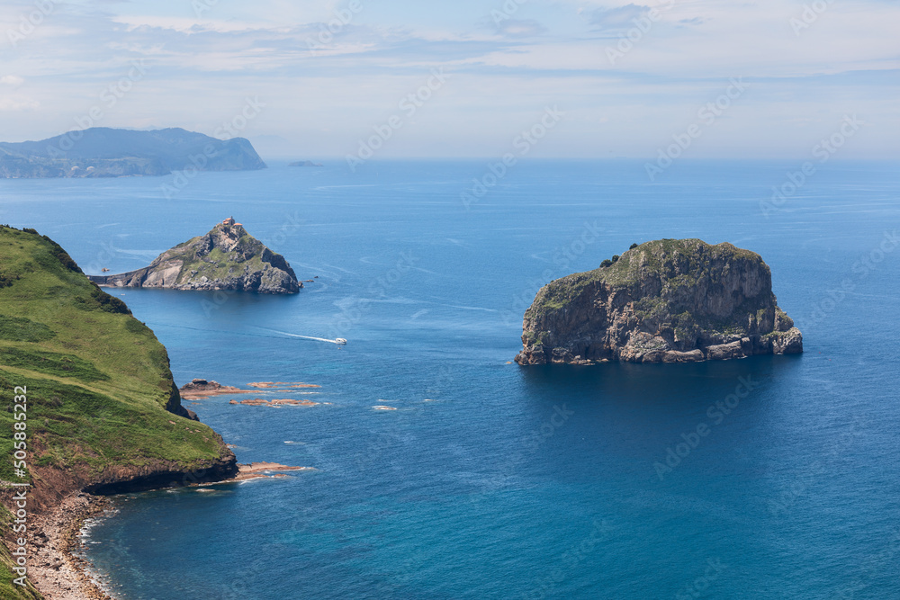 Emerald rocky coast, turquoise shallow waters of Bay of Biscay and two islands Isla de Aquech, Gaztelugatxe with hermitage dedicated to John the Baptist. Biscay, Basque Country