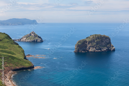 Emerald rocky coast, turquoise shallow waters of Bay of Biscay and two islands Isla de Aquech, Gaztelugatxe with hermitage dedicated to John the Baptist. Biscay, Basque Country