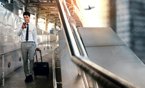 Smiling Passenger Businessman Using Mobile Phone while Walking with Suitcase in the Airport for a Business Trip. Full Length