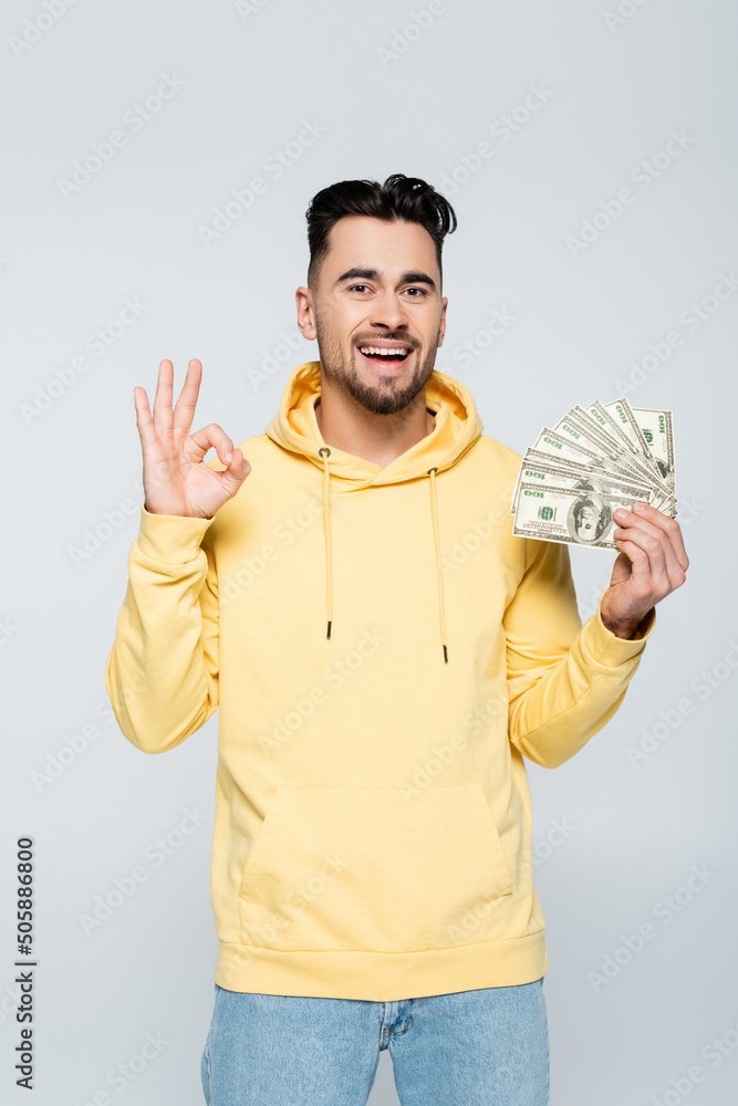 excited bookmaker holding dollars and showing okay sign isolated on grey. excited bookmaker holding dollars and showing okay sign isolated on grey.