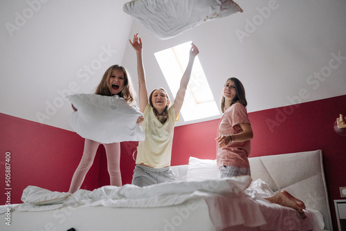 Lesbian family with their daughter playing in bed with a pillow and laughing photo