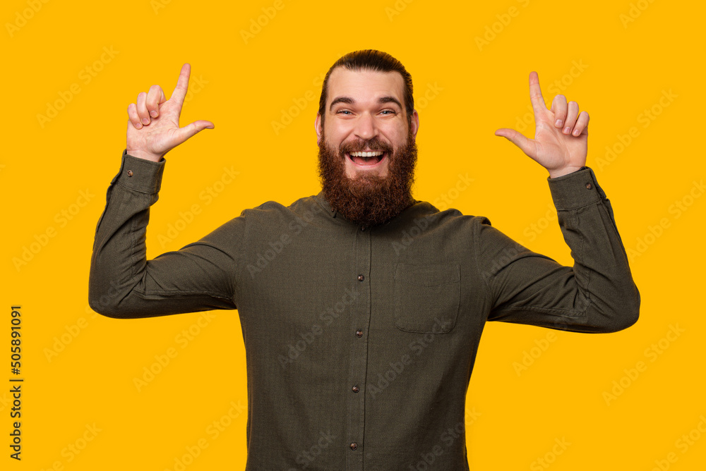 Portrait of a bearded man pointing up with both hands at the copy space. Studio shot over yellow background. Portrait of a bearded man pointing up with both hands at the copy space. Studio shot over yellow background.