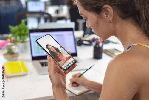 Caucasian businesswoman working on strategies online with female coworker through smart phone