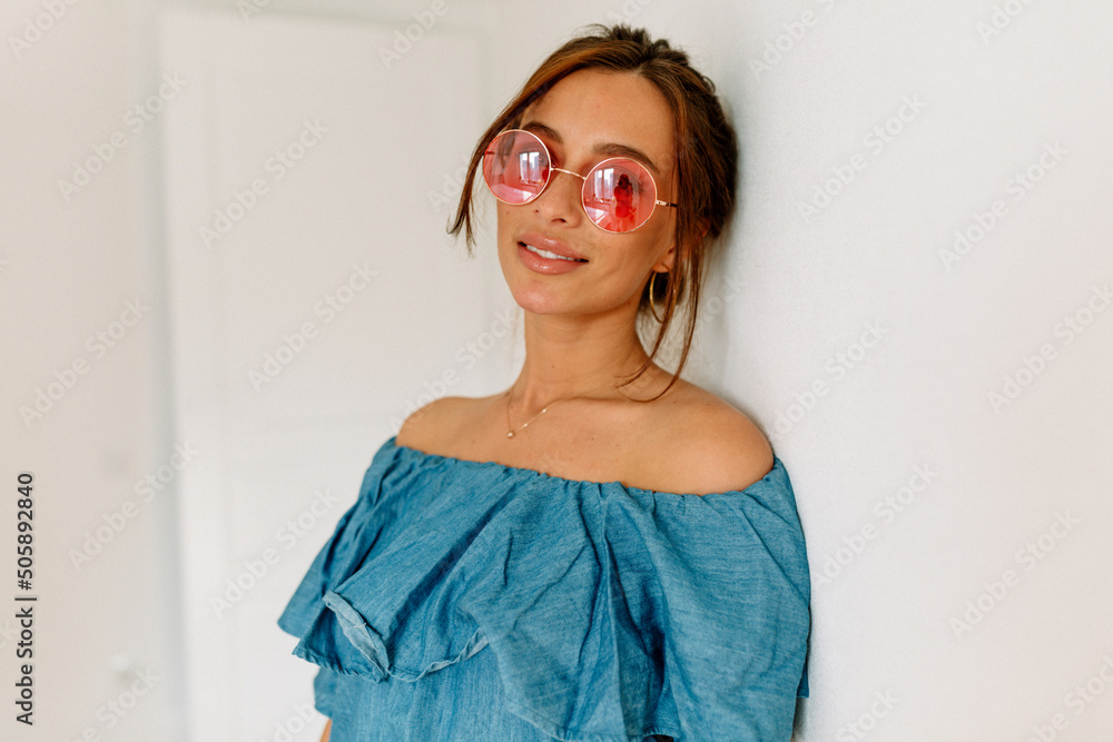 Adorable stylish tanned woman with dark hair wearing blue t-shirt and pink round glasses posing at camera over isolated background Adorable stylish tanned woman with dark hair wearing blue t-shirt and pink round glasses posing at camera over isolated background