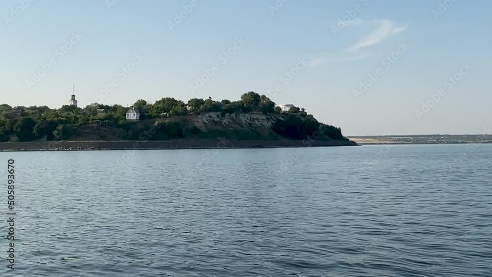 View from the water on coast of Tsimlyansk reservoir. In distance there is a steep coast, a rotunda and platinum against background of sky and sea waves. View from the water on coast of Tsimlyansk reservoir. In distance there is a steep coast, a rotunda and platinum against background of sky and sea waves.