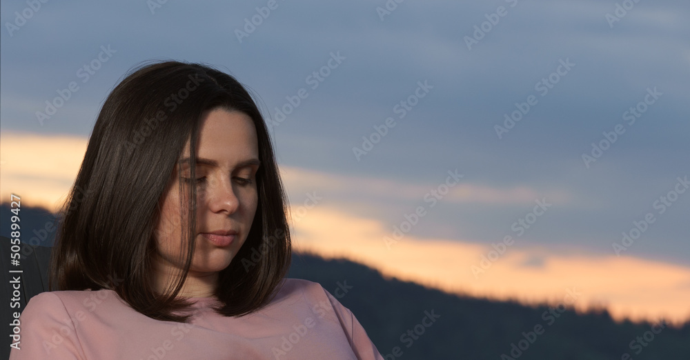 Head shot of Brunette woman looking down while sitting outdoor at sunset
