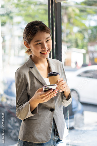 Successful young Asian woman talking on mobile phone during break from work. While standing near the copy space of your ad text or promotional material
