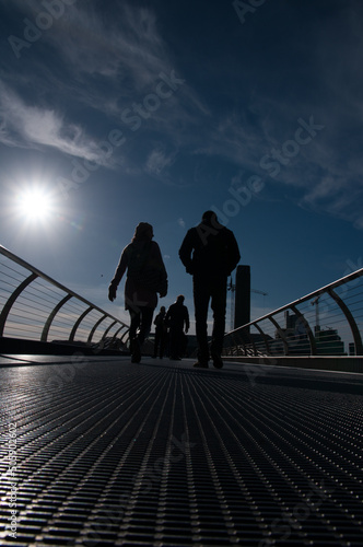 silhouettes of people crossing the Millennium Bridge in London - bright sun in blue sky. (ID: 505902602)