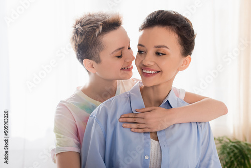 young bigender person with closed eyes embracing smiling partner.