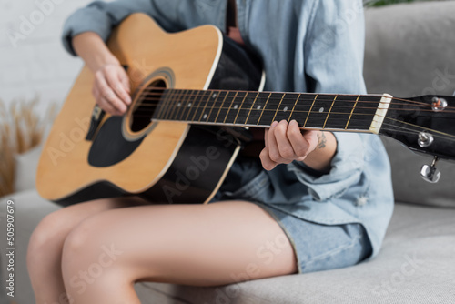 partial view of blurred woman playing acoustic guitar at home.