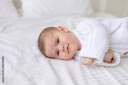 portrait of a newborn baby in a crib in a white warm jumpsuit on a white insulated cotton bed, cute baby close-up