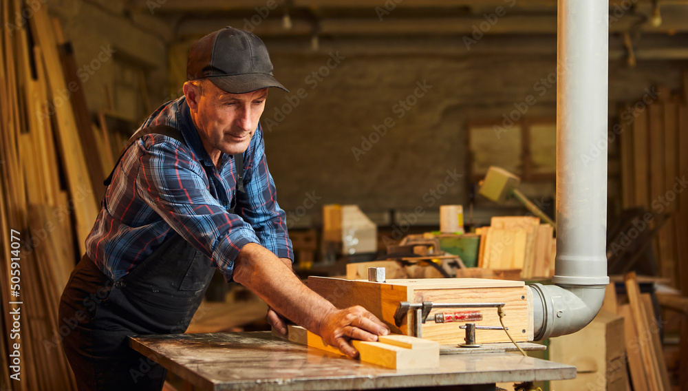 Senior carpenter in uniform works on a woodworking machine at the carpentry manufacturing Senior carpenter in uniform works on a woodworking machine at the carpentry manufacturing