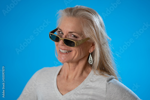 Portrait of mature woman posing like model in sunglasses gesture, isolated on blue background in studio. People emotions, lifestyle concept © Robert Peak