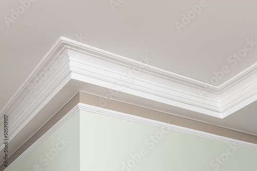 Angular ceiling skirting made of classic white crown moldings. Close-up detail of decoration in interior renovation. photo