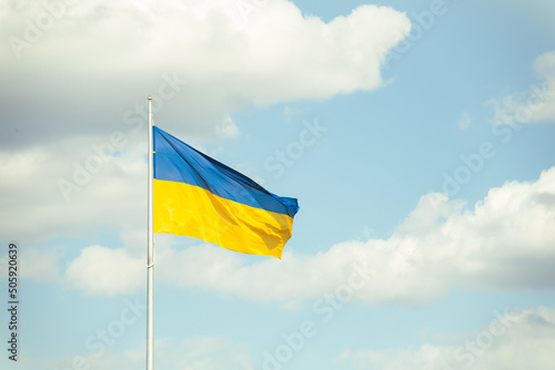 The big yellow and blue Ukrainian flag is waving in the wind as a symbol of independence and strength. Blue sky with white clouds in the background