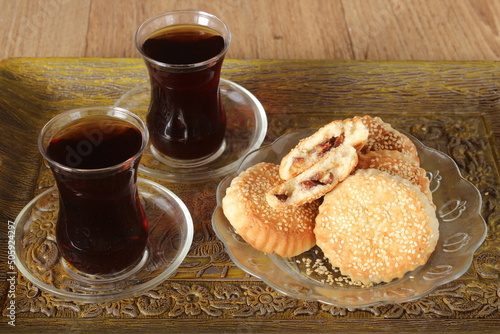 Date filled pastry with sesame known as ‘kombe’ in Hatay-Turkey and two glass black tea in tray on wooden table. Sitting view. photo