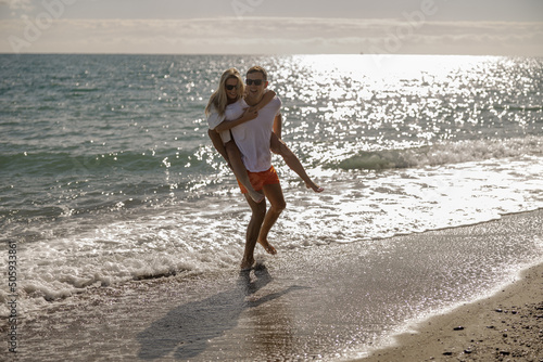Man carrying woman on his back, couple walking together along the sea coast