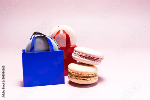 Sweet dessert colored macaroons with decor in the form of paper bags on a light pink background.
