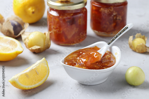 Homemade transparent physalis jam with lemon in bowl and glass jars on gray background