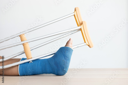 Blue ankle and foot splint Bandages on the legs from a young man's fall accident, Blue plaster on the ankle, Crutches assist in the walking of the patient. photo