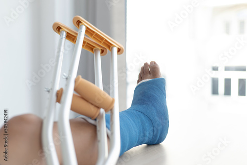 Blue ankle and foot splint Bandages on the legs from a young man's fall accident, Blue plaster on the ankle, Crutches assist in the walking of the patient. photo