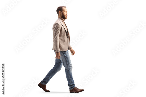 Full length profile shot of a man in a beige suit and jeans walking