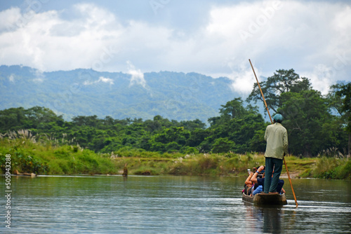 River trip in the Nepalese Jungle Chitwan National Park Nepal showing a man guiding a canoe with tourists along the river with a dramatic backdrop of high cloud covered mountains 