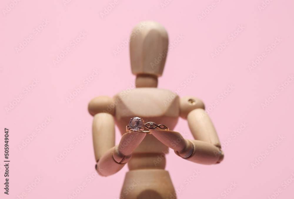 Wooden puppet holding diamond ring on a pink background. Marriage proposal concept Wooden puppet holding diamond ring on a pink background. Marriage proposal concept