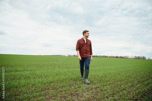 Young farmer stands in the green field checking and waiting for harvest to grow.