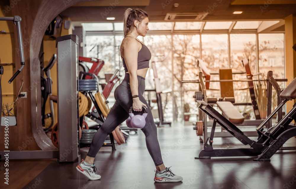 Fit woman practices lunges with kettlebells in her hands in the gym. Leg workout Fit woman practices lunges with kettlebells in her hands in the gym. Leg workout