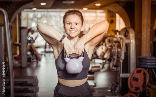 Smiling fit woman doing kettlebell rows to the chin in modern gym