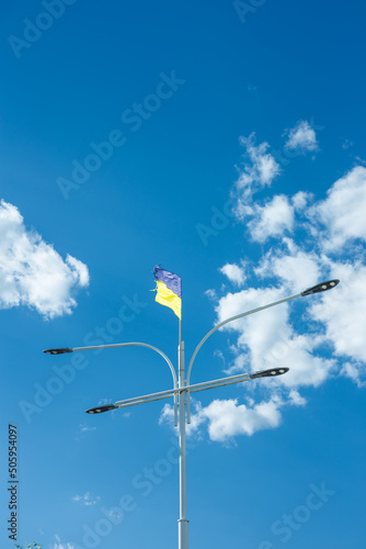 Ukrainian yellow and blue national flag on street lamp fluttering on blue cloudy sky background, vertical shot